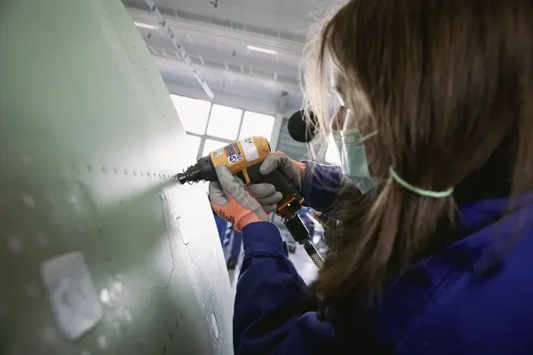 Apprenti posant des rivets avec un marteau à riveter à système antivibratile