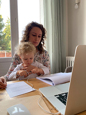Photo représentant une salariée en télétravail à son domicile, assise devant son ordinateur avec son enfant sur les genoux Photo représentant une salariée en télétravail à son domicile, assise devant son ordinateur avec son enfant sur les genoux